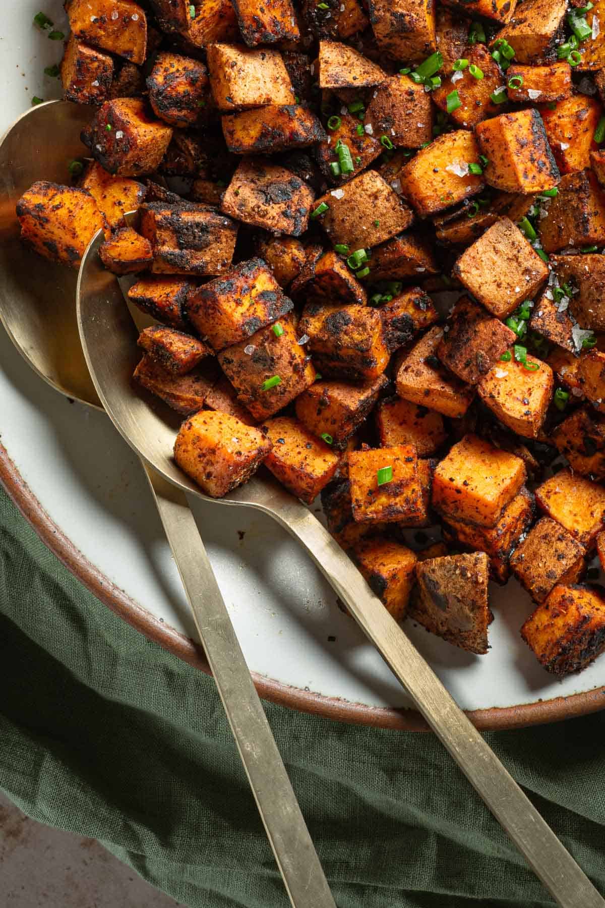Up close photo of sautéed Sweet Potatoes in a bowl with serving spoons.