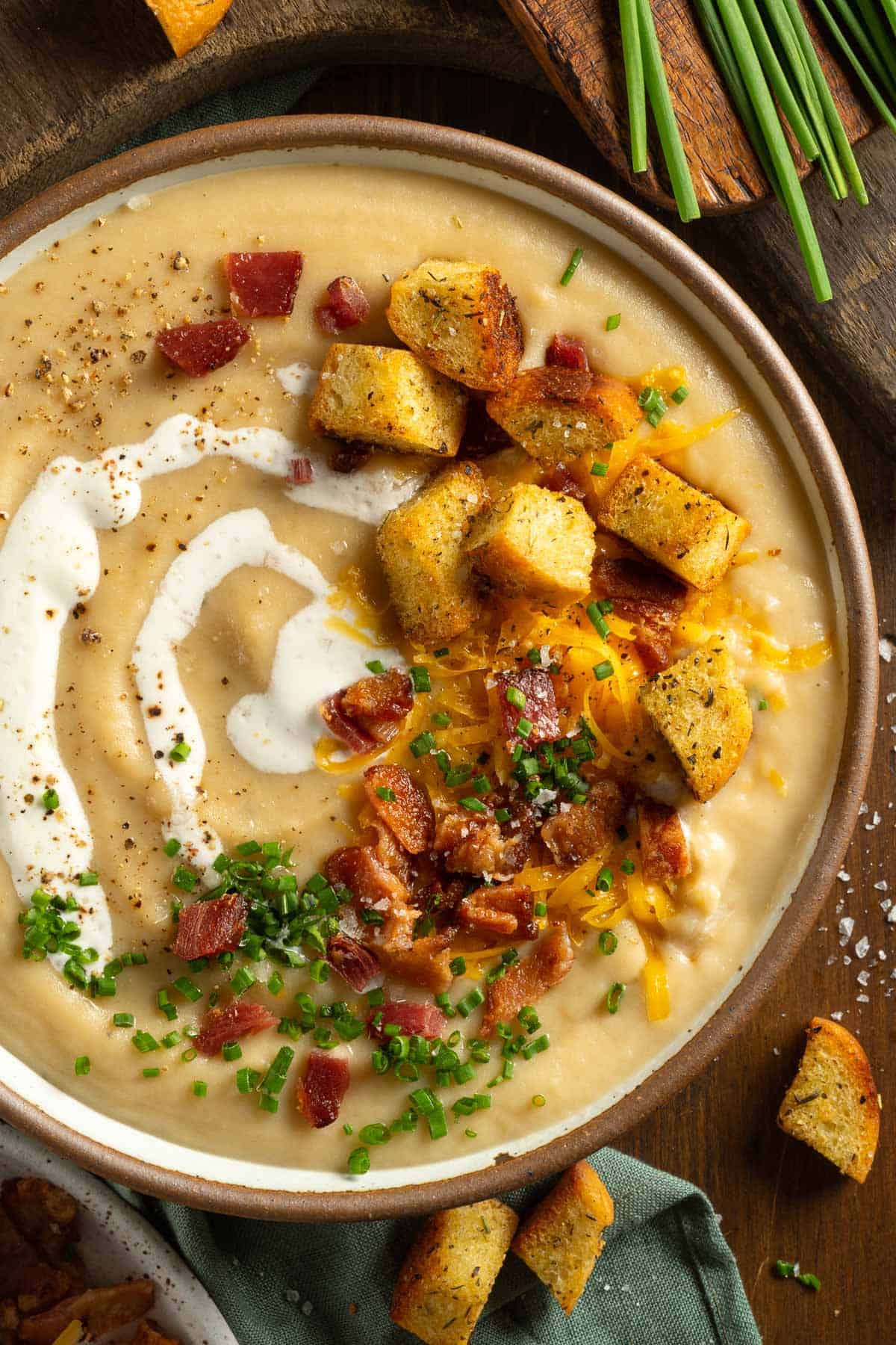 An up close bowl of potato soup topped with bacon, cream, chives, and croutons.