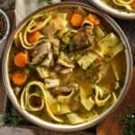 A bowl of homemade chicken noodle soup with parsley, dill, and lemon.