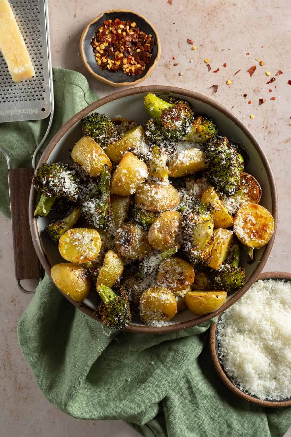 Roasted potatoes and broccoli in a serving bowl topped with parmesan.