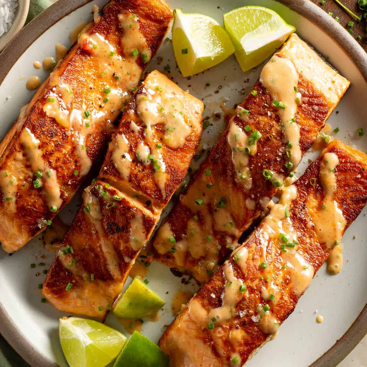 Salmon drizzled with bang bang sauce topped with lime juice and chives on a plate.