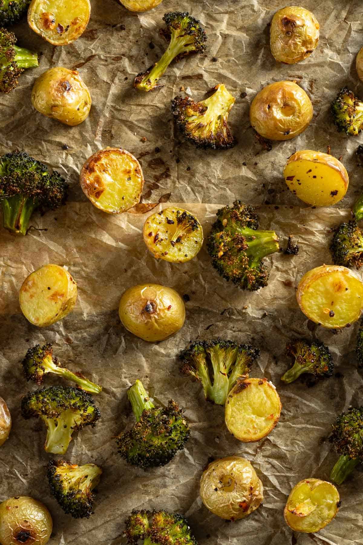 Up close roasted broccoli and potatoes on a baking sheet.