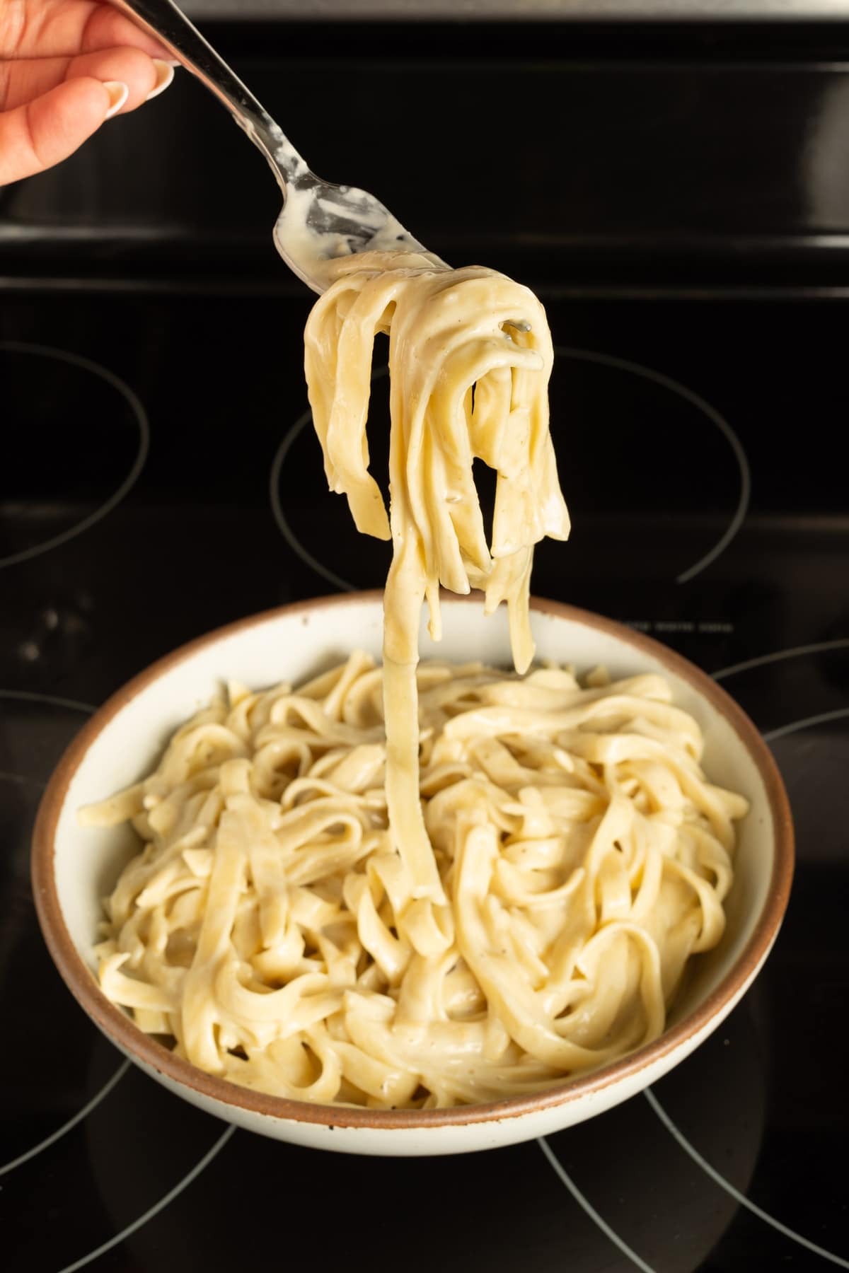 A fork holding a scoop of fettuccine alfredo over a bowl.