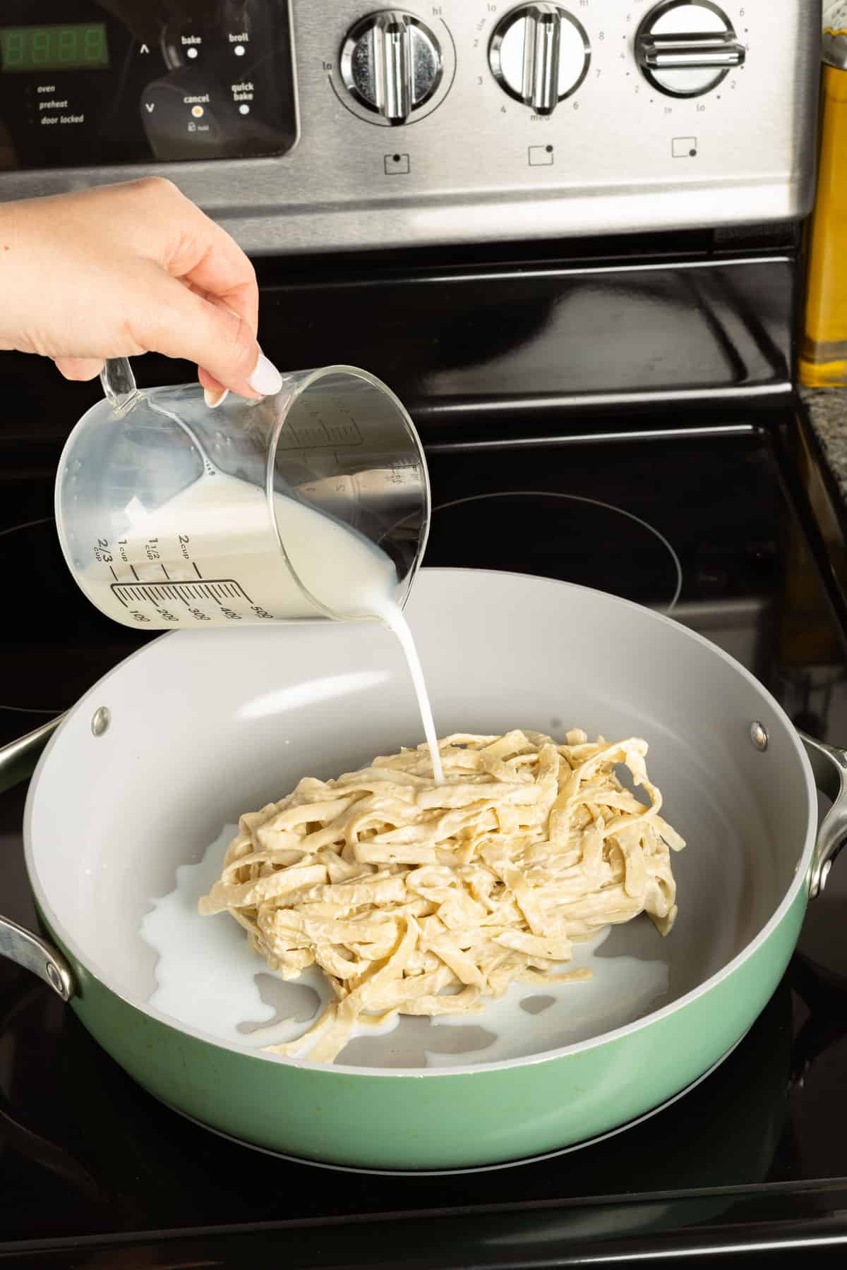 Pouring milk into a pan with alfredo pasta.