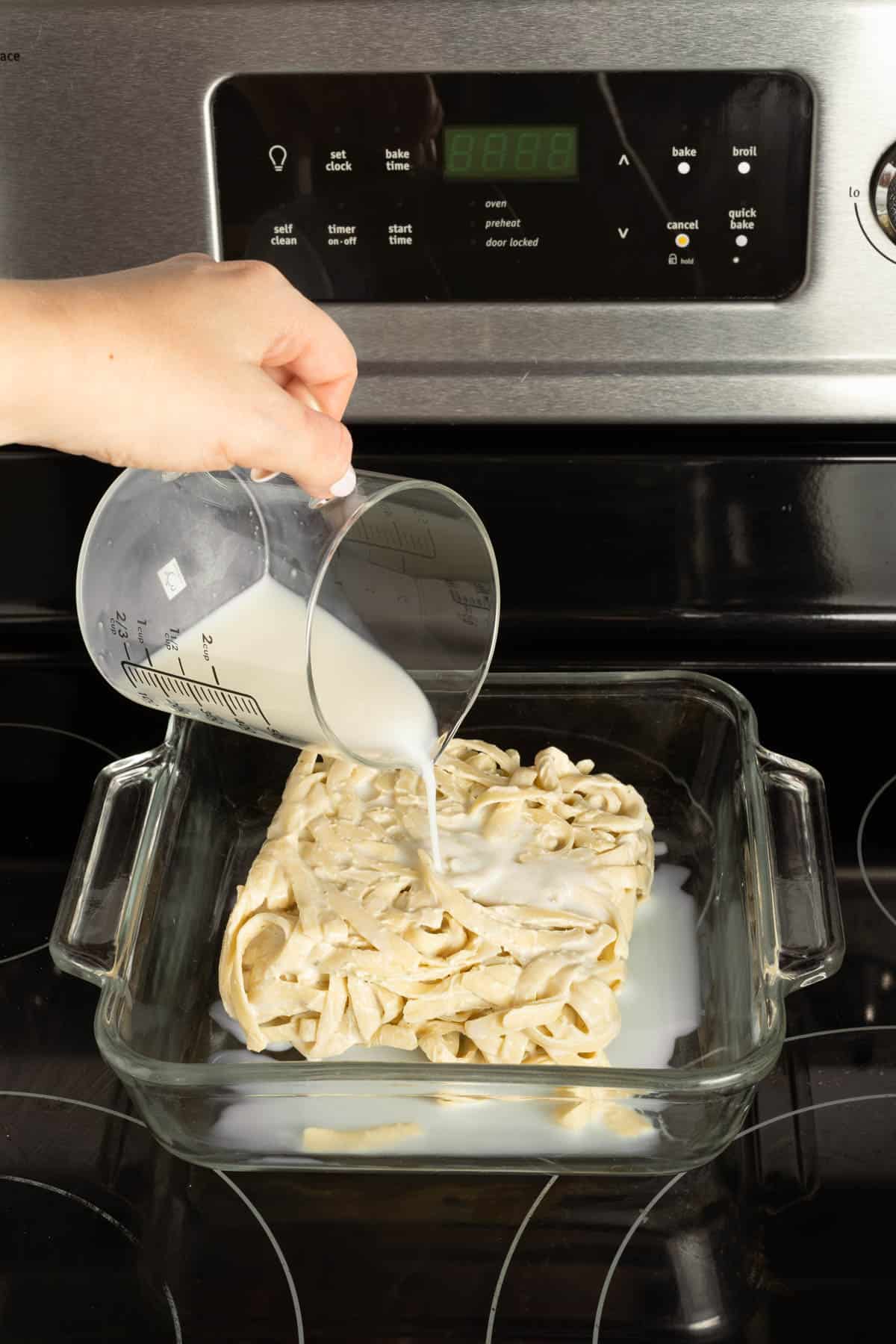 Pouring milk over alfredo to reheat it.