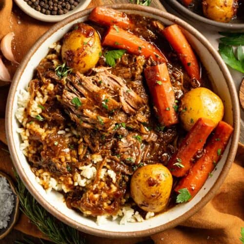 A bowl of tender pot roast with fresh herbs, carrots, and potatoes.
