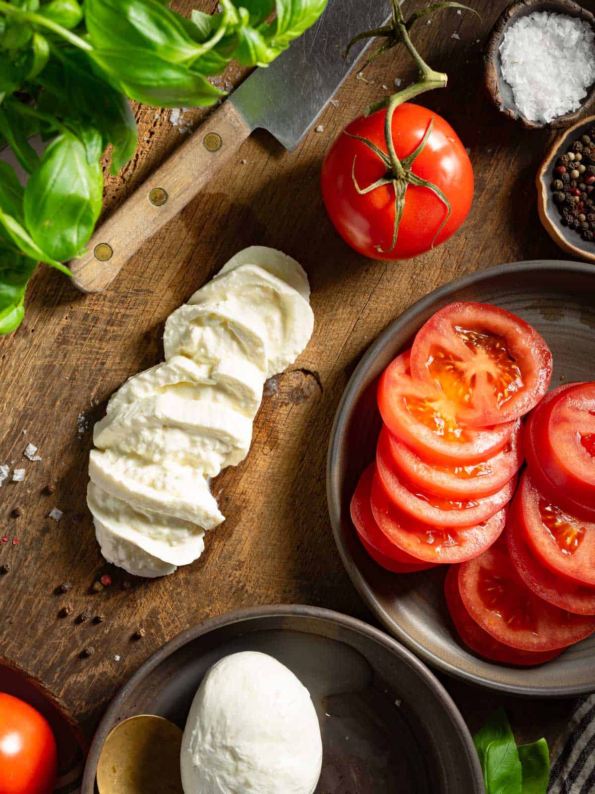 Sliced burrata and tomatoes on a cutting board.