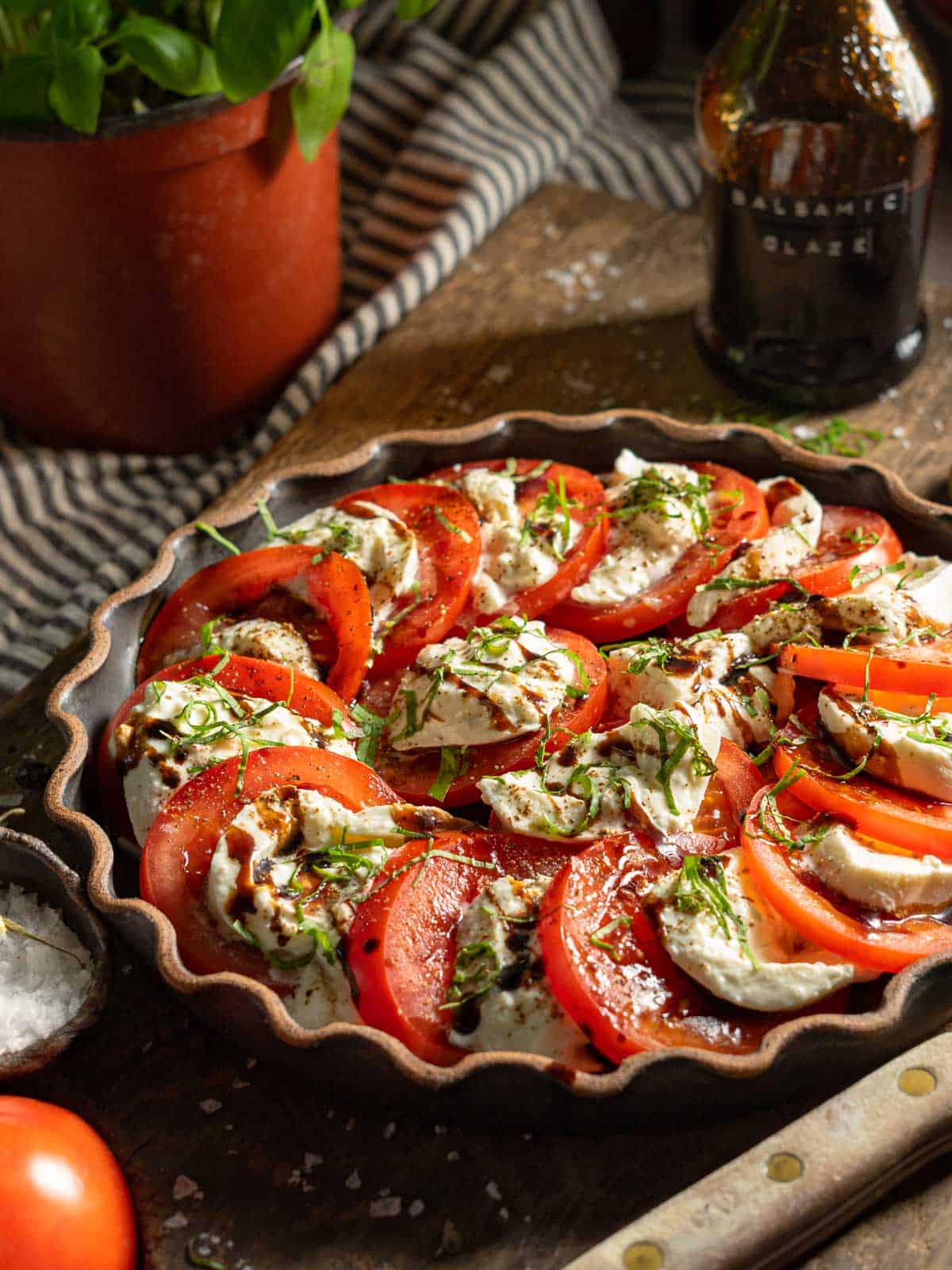 Burrata caprese salad on a serving platter with a bottle of balsamic glaze behind it.