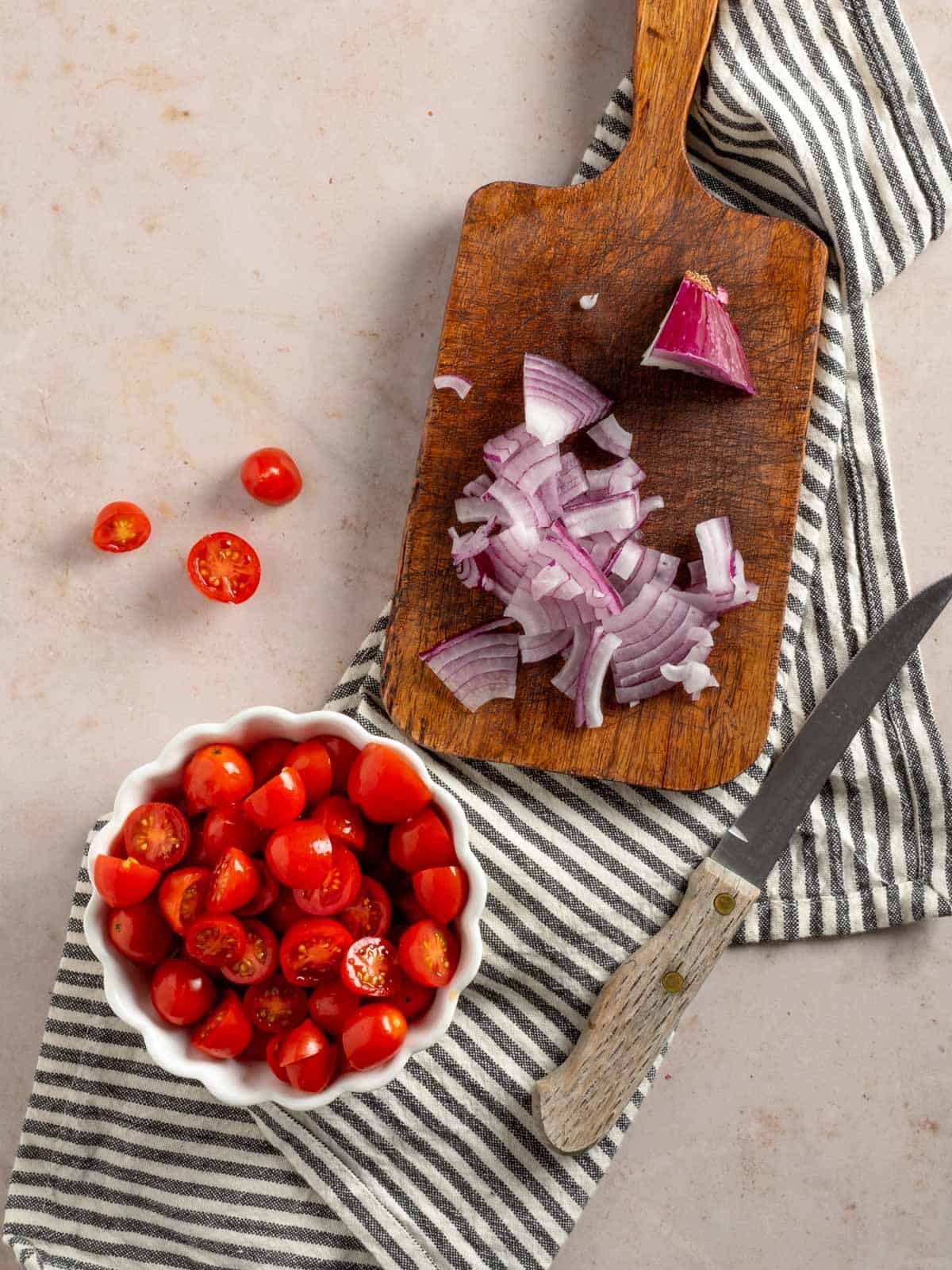 Chopped tomatoes in a bowl and diced red onion on a cutting board.