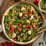 Orzo pasta salad with pesto, tomatoes, mozzarella, pine nuts, arugula, and balsamic glaze in a serving bowl.