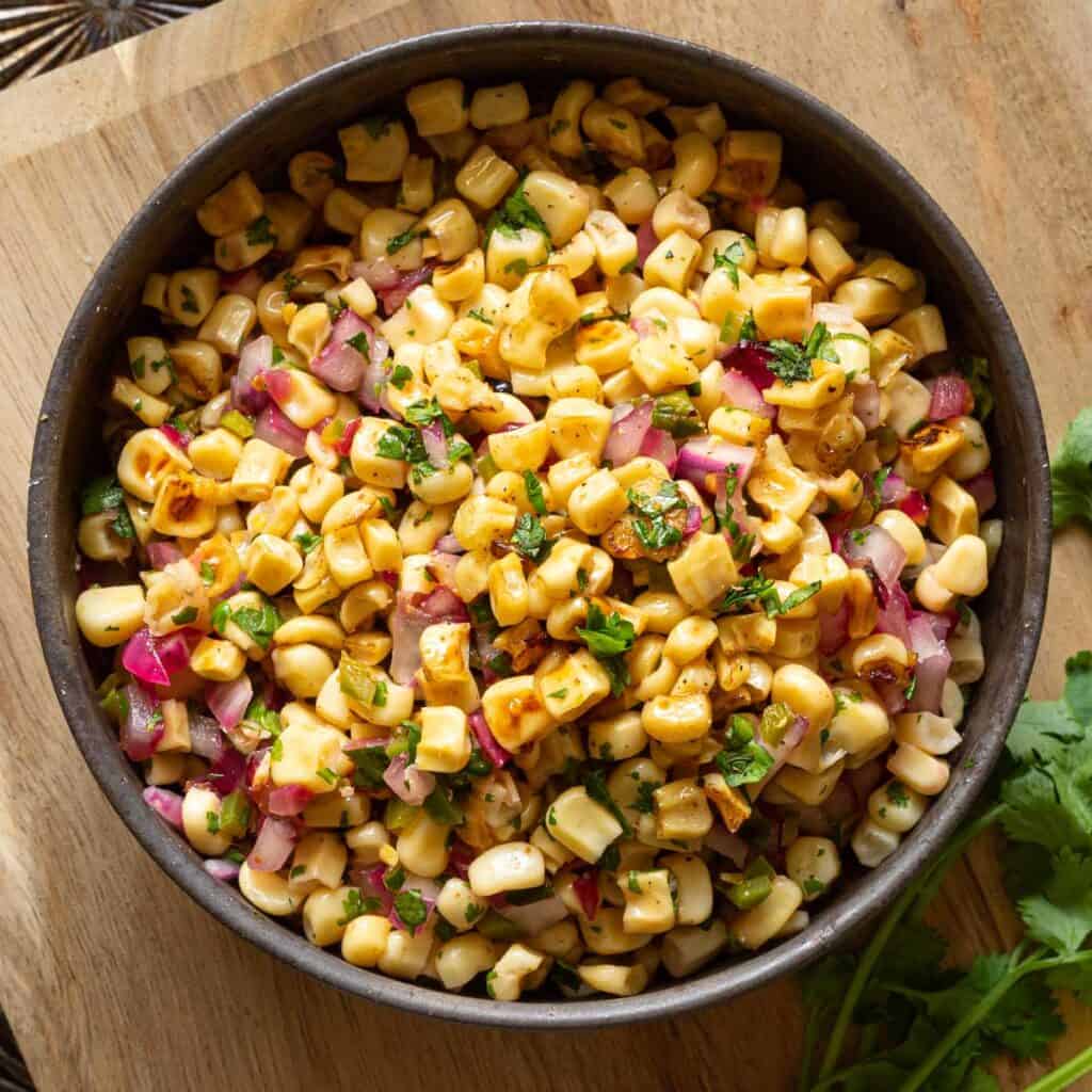 Up close view of a bowl of roasted chili corn salsa with charred corn, red onion, pepper, and cilantro.