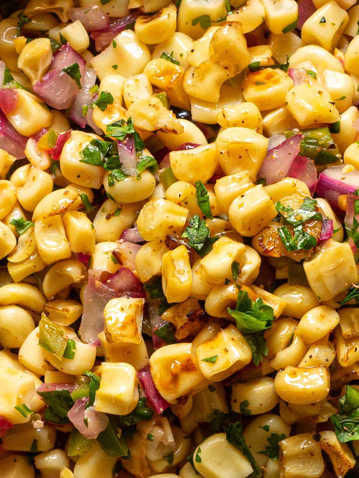 Zoomed in view of charred corn mixed with jalapeños, red onions, and cilantro.