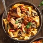Bowl of creamy cajun salmon alfredo pasta with sun dried tomatoes, red peppers, and mushrooms.