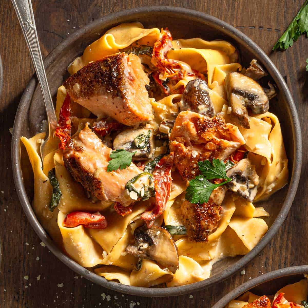 Bowl of creamy cajun salmon alfredo pasta with sun dried tomatoes, red peppers, and mushrooms.