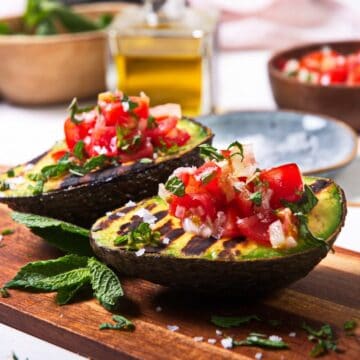 Grilled avocados with tomatoes on a cuttingboard.