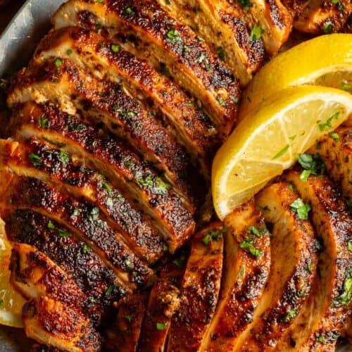 Up close sliced blackened chicken breasts with parsley and lemon.