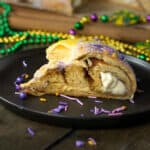 King cake on a plate with purple sprinkles and Mardi Gras beads.