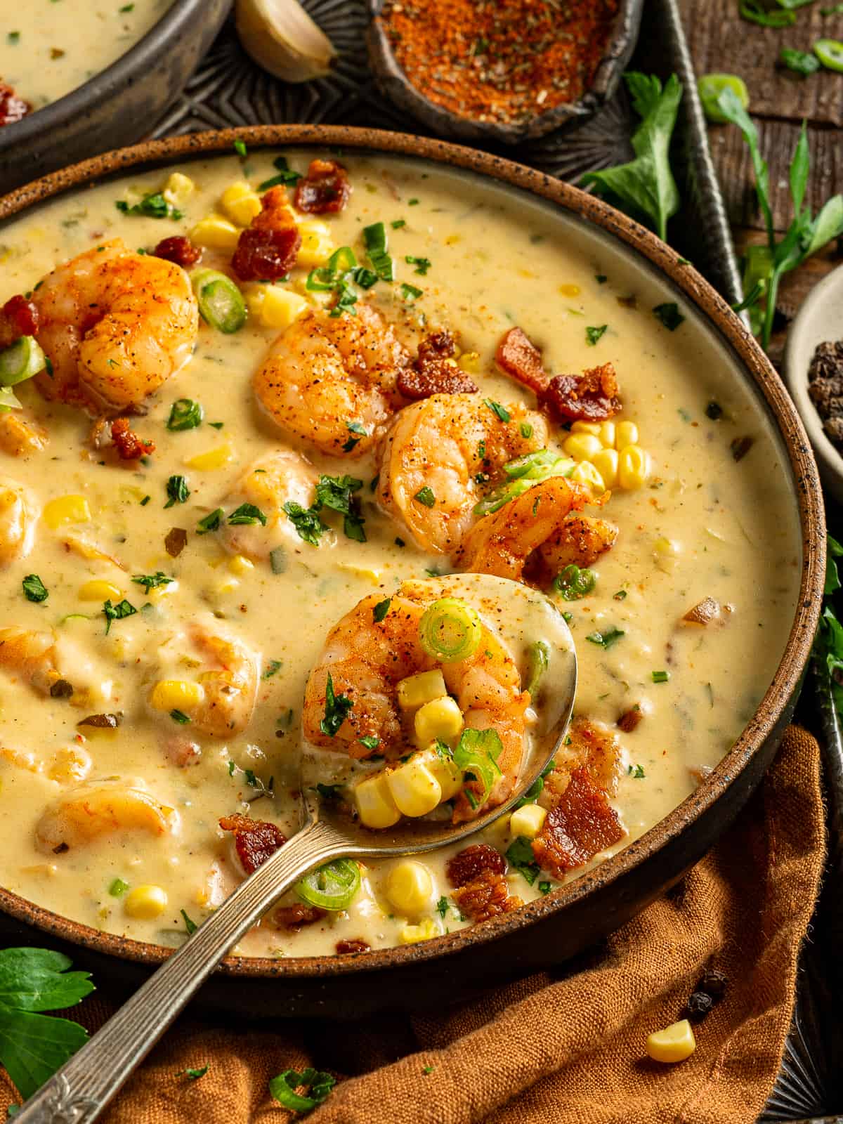 A bowl of creamy shrimp and corn bisque with bacon and green onions and a spoon scooping a bite.