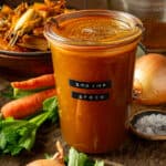 A container of homemade shrimp stock next to mirepoix on a cutting board.