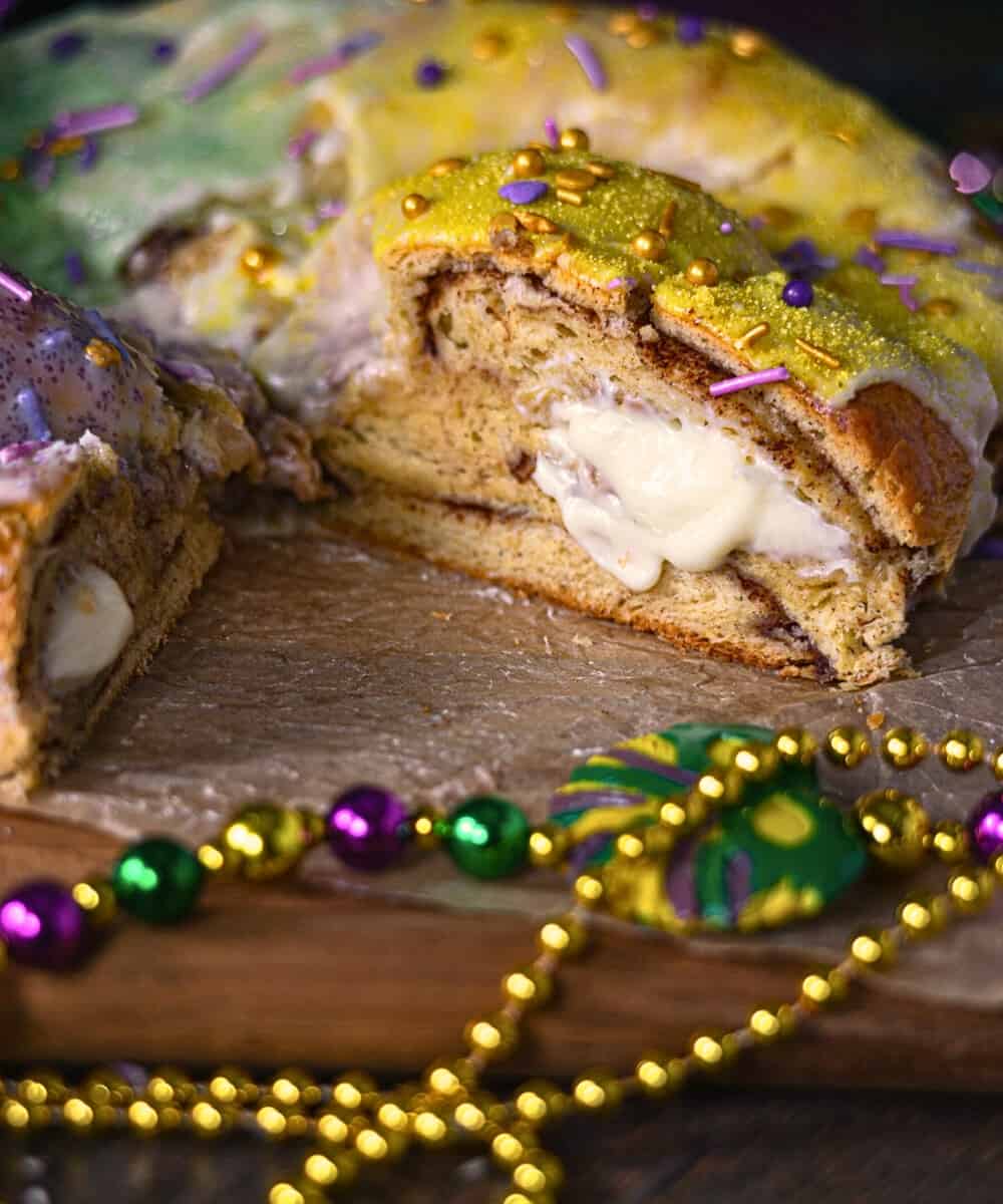 This photo shows New Orleans Cream Cheese King Cake on a cutting board, sliced, showing the inside filling 