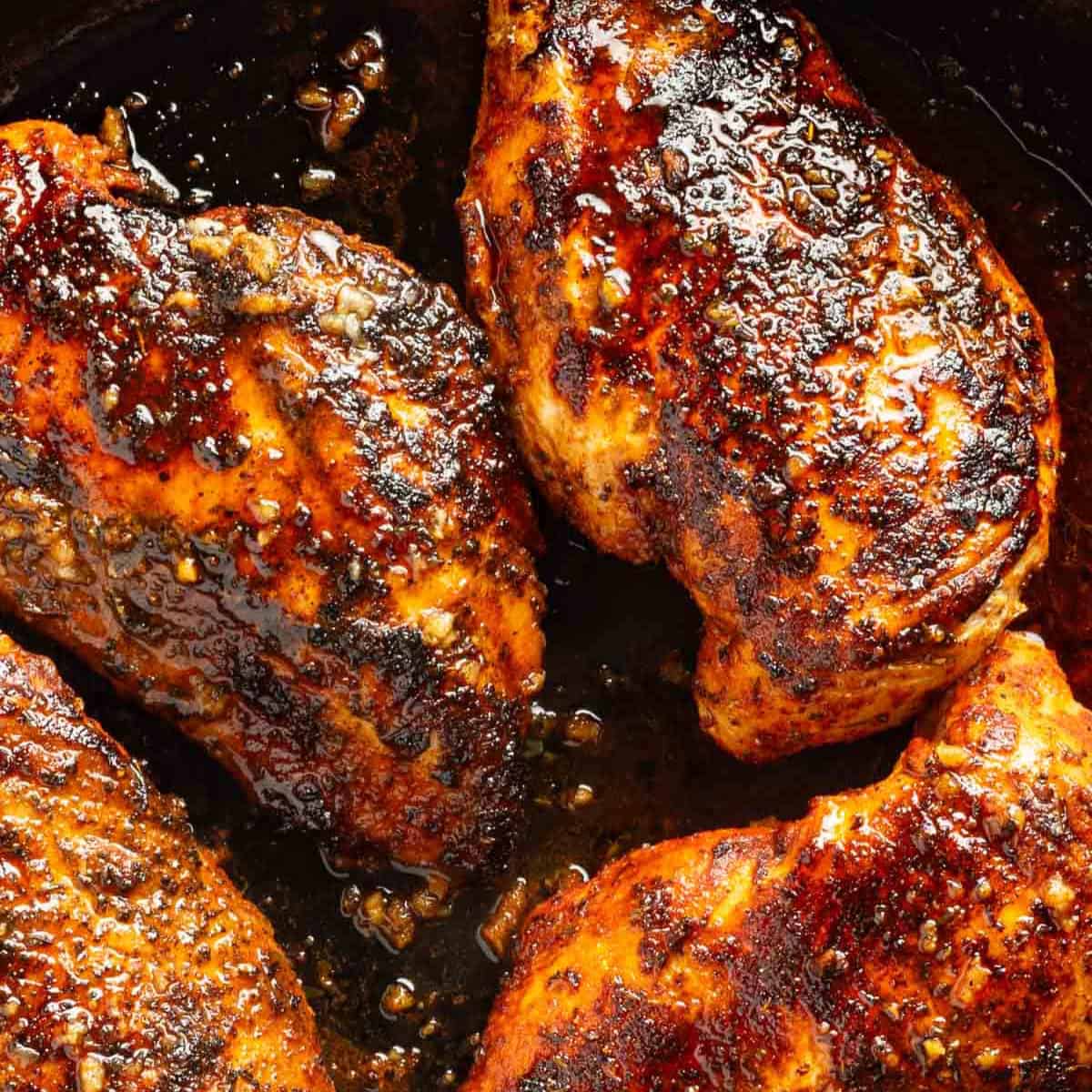 Blackened chicken breasts in a skillet with garlic butter.