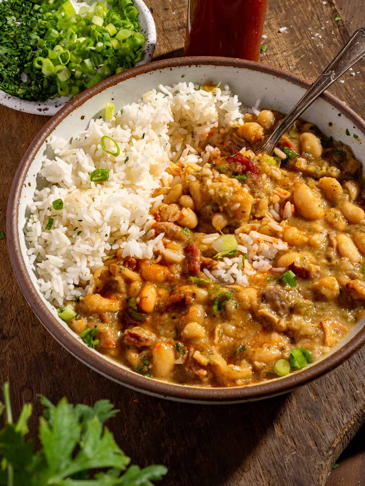 A bowl of white beans over rice with hot sauce.