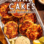 A tray of crab cakes sprinkled with parsley and a side of crab cake sauce.