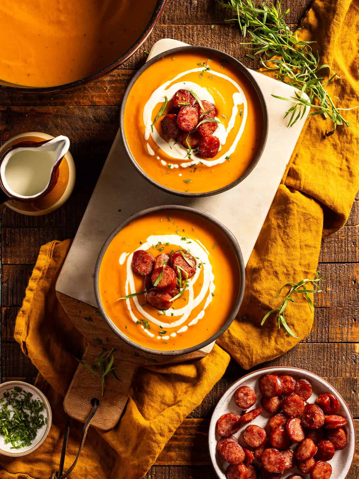 Two bowls of butternut squash soup with sausage on a serving tray.